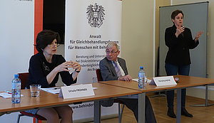 Ursula Frohner, Hansjörg Hofer und Barbara Gerstbach als Gebärdendolmetscherin vor einem Rollup des Behindertenanwalts